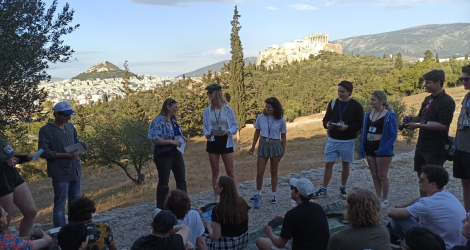 University students reenact ancient democratic assembly on Pnyx Hill with Acropolis behind.